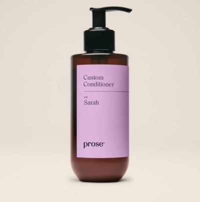 A personalized bottle of Prose custom conditioner with a black pump and sleek amber and purple label. The label reads “Custom Conditioner” with a personalized name, highlighting its tailored haircare formulation.