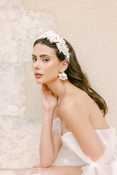 Candid image of a bride sitting on a stone bench turning slightly to the camera with one hand under her chin