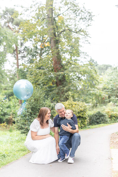 A mum and dad knelt down with their son and a blue balloon outsite.
