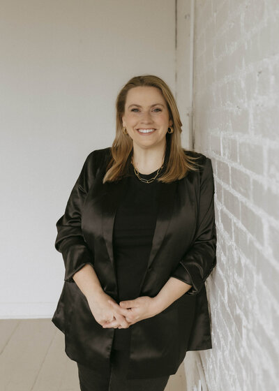 Renee in black blazer leaning on white wall