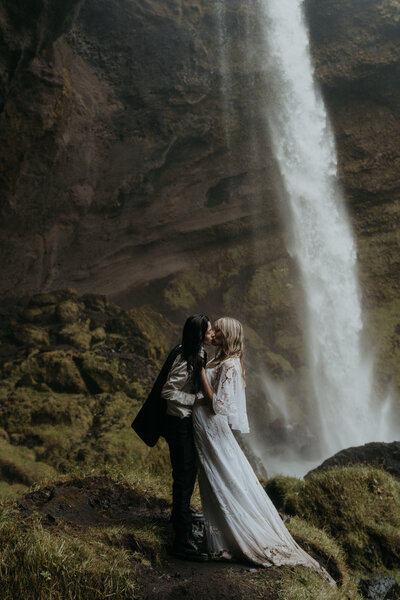 Bride wearing pink wedding dress and flowers in hair faces groom wearing green suit jacket looking into each other's eyes in Fern Canyon surrounded by light rays and trees taken by California elopement photographer Kasey Mantiply