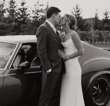 A couple kissing in front of a car posing for a photo
