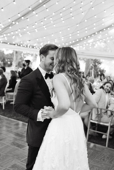 Tented wedding reception in Ontario's Prince Edward County. Couple dances under twinkling lights on a dancefloor surrounded by loved ones.