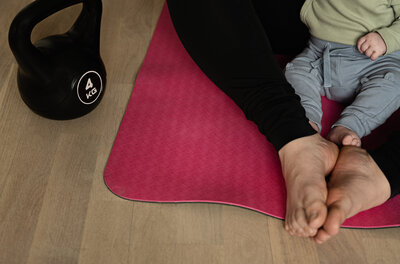 Füsse von einer Frau und einem Baby auf einer Fitnessmatte beim Rückbildungskurs nach der Schwangerschaft