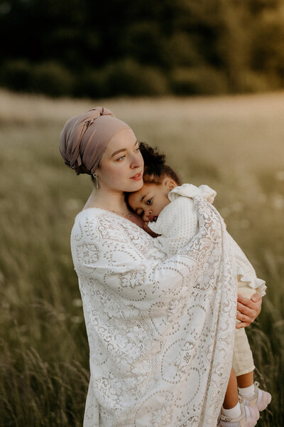 en mamma i hijab håller om sin dotter på ett fält