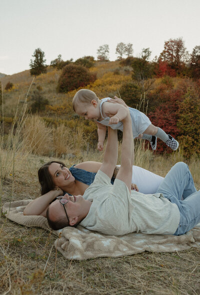 A husband and wife facing away from the camera. The husband is holding their baby up above their heads.