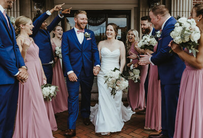 A bride and groom walk through their cheering wedding party