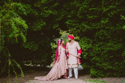 A sikh bride and groom smiling at each other under a tree tunnel at the planting fields arboretum after their glen cove wedding in ny