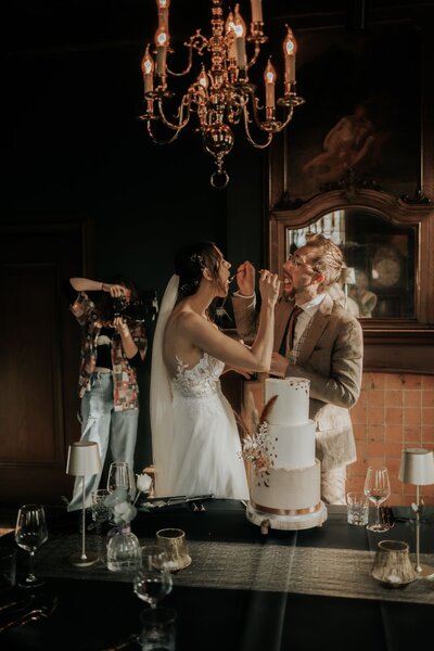 Een bruidspaar dat taart eet en ondertussen op de foto gezet word door een trouwvideograaf