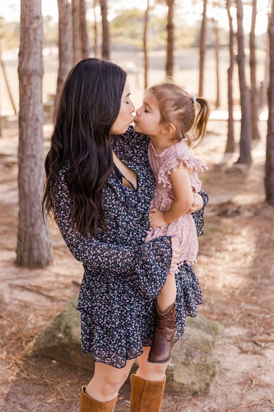 Mom and daughter kissing in the woods, by Claire Thom