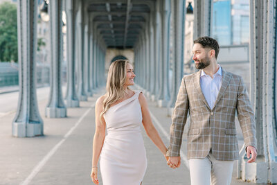 Couple holding hands and looking at each other while walking through Paris near the Eiffel Tower and Montmartre during a romantic couples photoshoot.