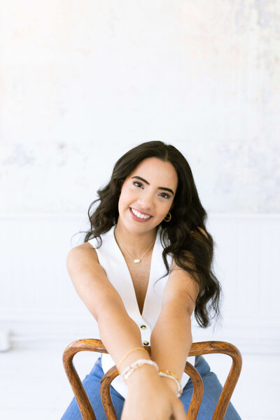 girl with dark hair sitting in a wooden chair wearing a white short and a photography studio