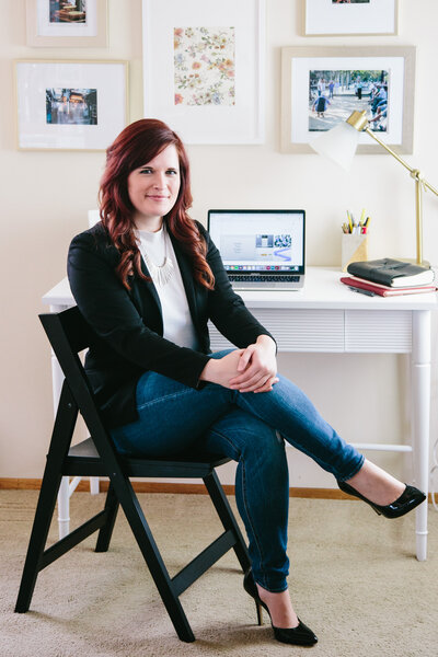 A professional woman sitting at a desk, posing for her branding photos.