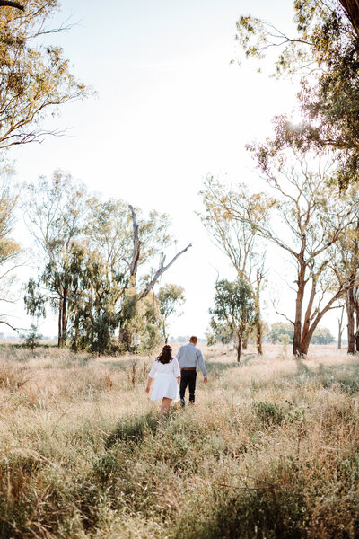 engaged couple walking through a field