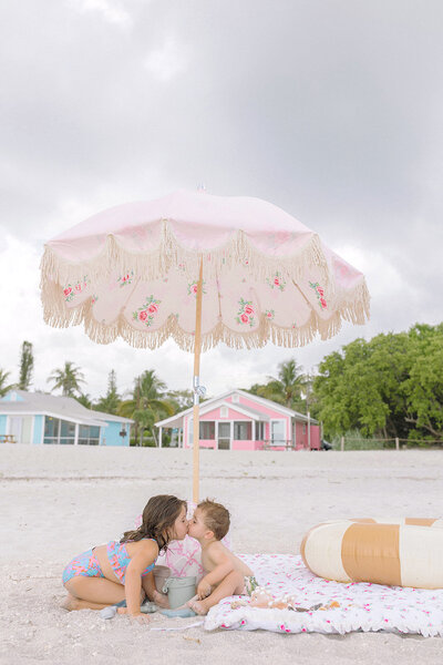Two kids giving each other a kiss while sitting on the beach