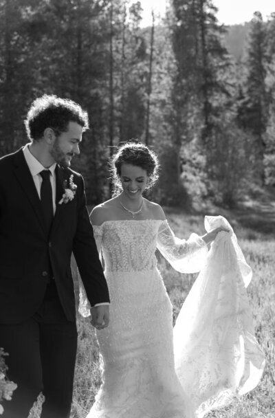 Romantic portrait of bride and groom walking through a meadow at golden hour during their Camp Hale wedding in Vail, Colorado