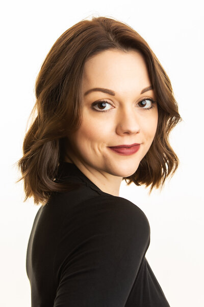 A woman sits backwards on a chair smiling at the ground