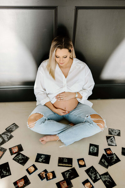 fine art maternity portrait session of expectant mother sitting against black wall looking at sonogram images