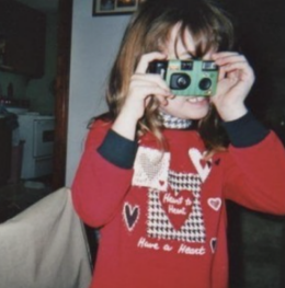 Younger Katelyn holds a camera while smiling.