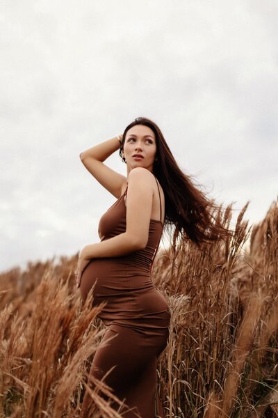 Miami photographer captures striking maternity portrait in a natural outdoor setting with tall grass and wind
