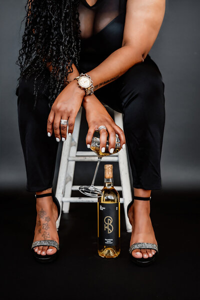 a photo of a woman holding a glass of wine with the full bottle next to her