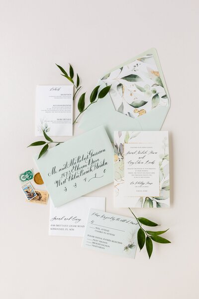 Elegant wedding stationery flat lay with sage green accents, olive branches, and script lettering