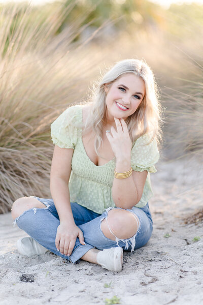 girl sitting on the beach in a green top and jeans