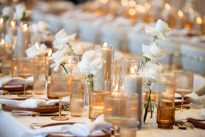 A timeless elegant table featuring the Pantone color of the year,  lined with cream pillar candles, amber and brown votive holders, and single double cream roses in  clear  bud vases spanning the length of the table