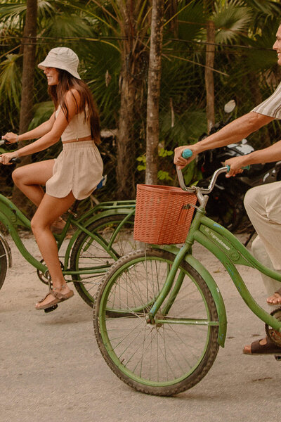 Couple biking through downtown Tulum on green bicycles, capturing playful pre-wedding photos in the streets.