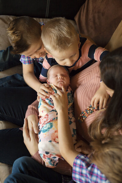 Mom holding newborn baby girl as her 3 brothers check her out.
