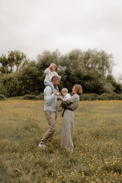 een gezin staat in een bloemenveld te knuffelen tijdens een fotosessie in Bonheiden.