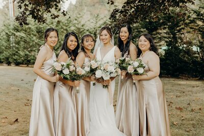 Bride and her bridesmaids in silk cream dresses holding wedding bouquets