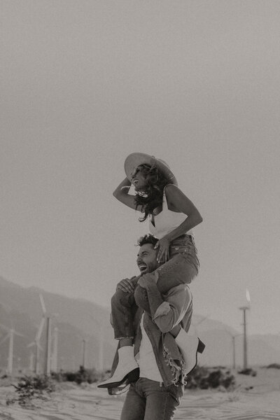 Wife piggy back riding on her husbands shoulders while they're both laughing. Photo taken from a lower angle.