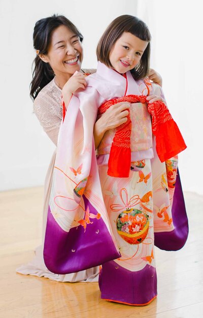 Sachiko dressing a young girl in a vibrant Shichi Go San kimono during a private fitting session for kimono rental in Los Angeles | ロサンゼルスで七五三の女の子に着物を着付けるサチコ。プライベート着付けセッションでの一枚。着物レンタルに最適
