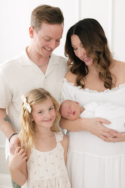 Portrait of a beautiful family of four dressed in light neutral clothing as they snuggle their newborn baby in a bright louisville kentucky studio taken by missy marshall