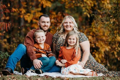 Family sitting on blanket in front of fall leaves