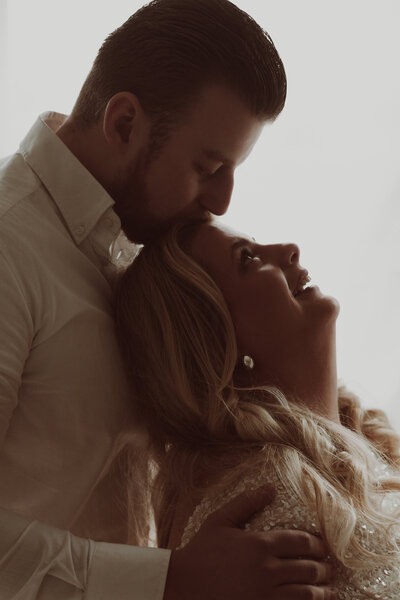 Een man en vrouw omarmen elkaar voor een witte achtergrond, stralend van liefde en verbondenheid.