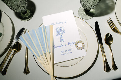 Luxury editorial flat lay featuring blue wedding fans, calligraphy menus, and heirloom china at a fine art Austin wedding celebration.