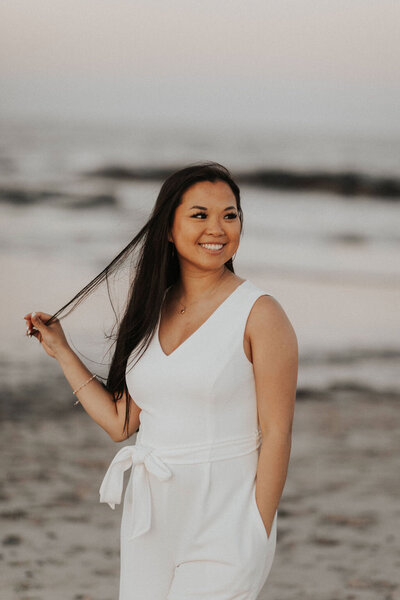Wedding and elopement photographer smiles and looks to the side on the beach at sunset