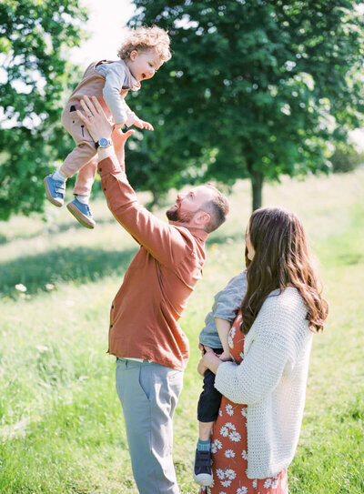 family of two little children playing while dad is holding one children above his head and mother holding second child and looking at them