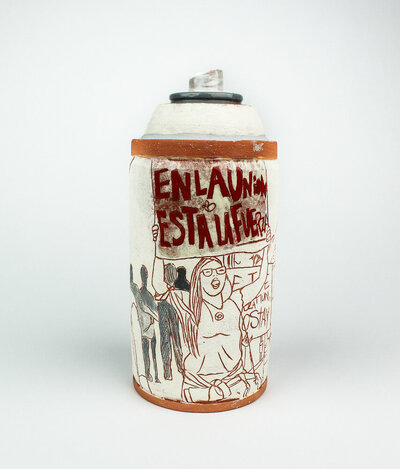 A ceramic jar in the shape of a spray paint can is decorated with imagery of a protester holding up a sign that reads en la union esta la fuerza