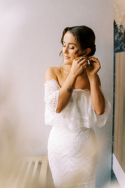 photo of bride putting on earrings while wearing her bridal gown taken by Jackson Hole Wedding Photographer