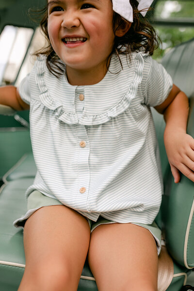 A little girl wearing a light blue striped button shirt with ruffle collar back to school