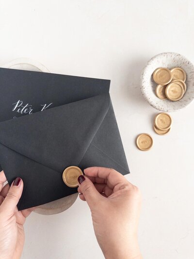 DC calligrapher and wedding stationery designer assembling custom wedding invitation black envelopes with gold wax seals