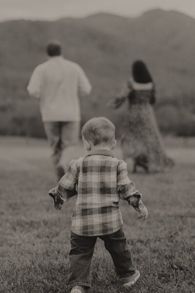 In a black and white photo, a mother and father run away while their young son follows them.