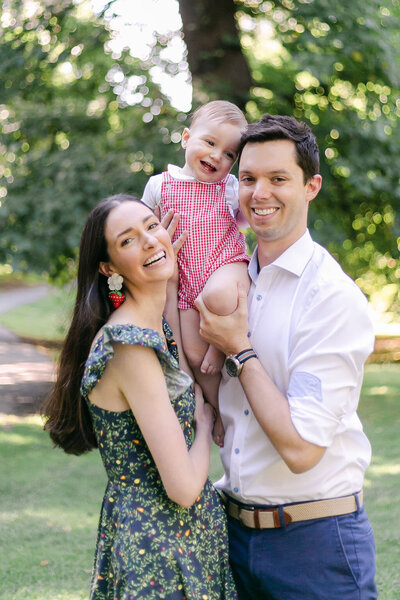 A mother and father hold their smiling toddler between them - photo by Rochester NY newborn photography service Emi Rose Studio.