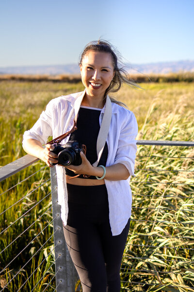 Bay Area Lifestyle Photographer - Ellobelle Photography Family Photographer posing with Canon camera and genuine smile by tall reeds