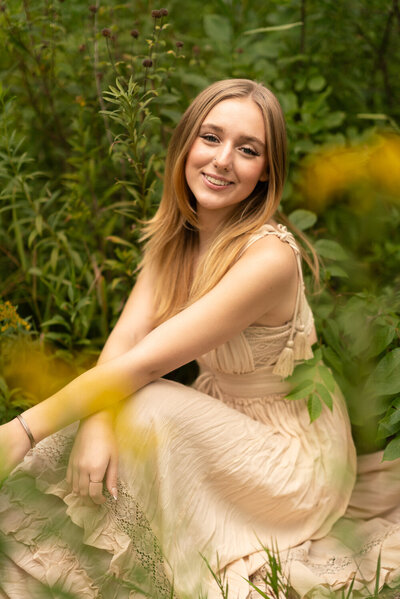 Senior girl stands in a flower field in a pink sundress.