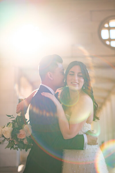 Bride and groom embrace in golden sunlight with lens flare