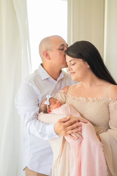 Indoor family photography of dad kissing mum holding newborn girl in Brisbane Studio
